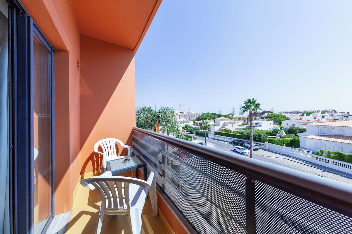 A balcony with a table and chairs, overlooking a residential area with buildings and palm trees.