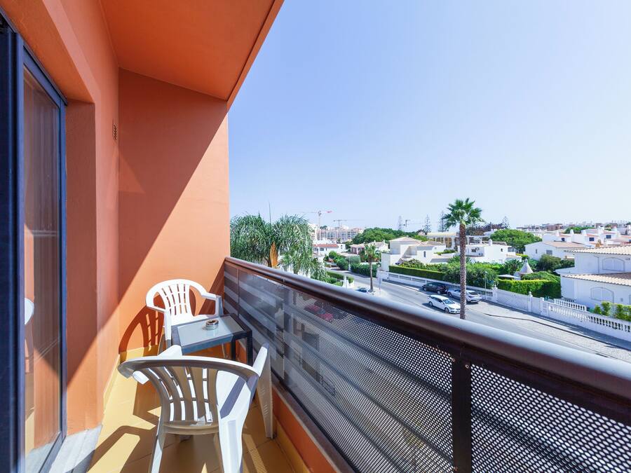Un balcón con mesa y sillas, con vistas a una zona residencial con edificios y palmeras.