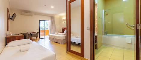 A hotel room with two beds, a desk, a chair, a bathroom with a bathtub, and a shower.