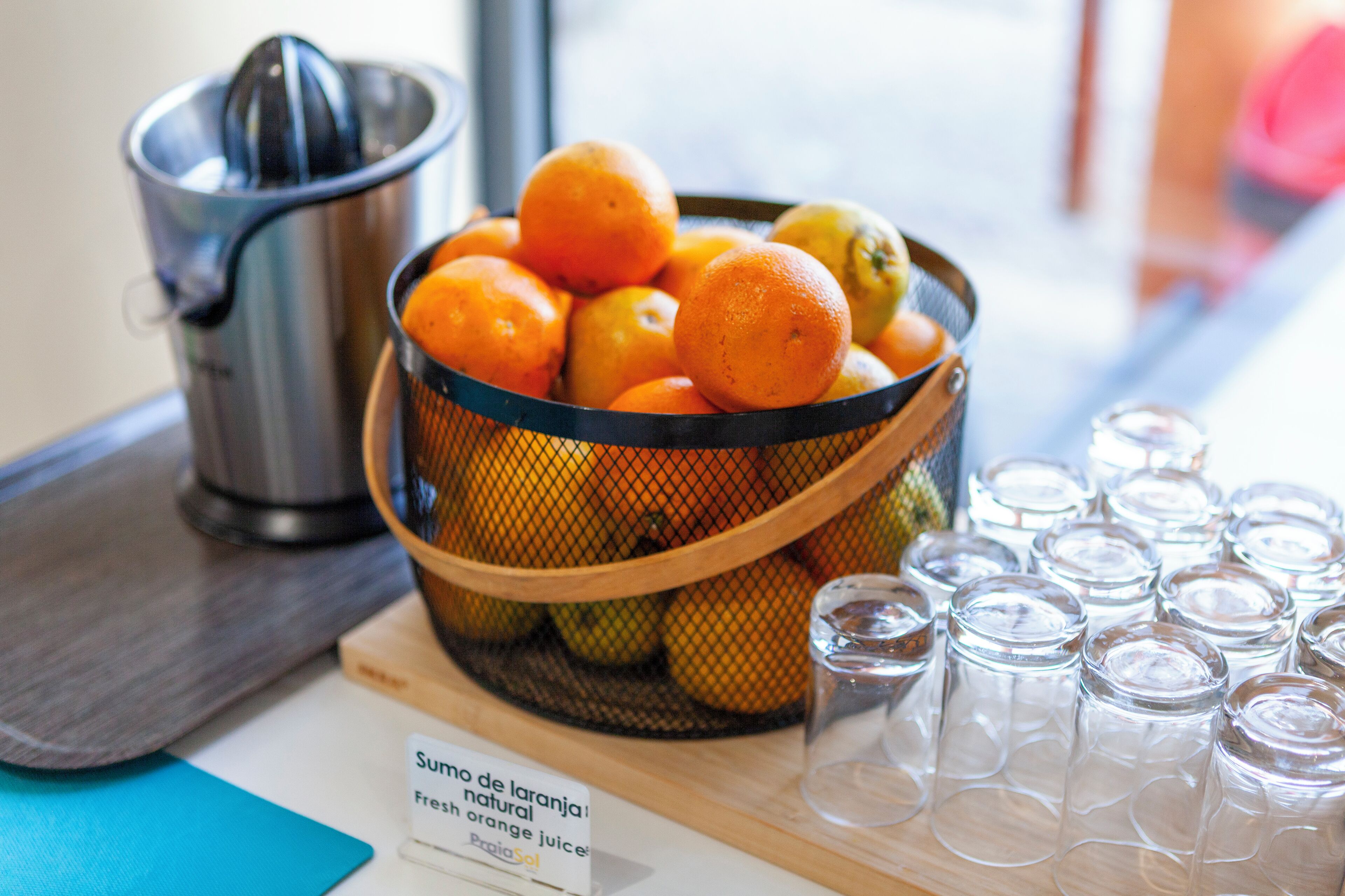 A basket of oranges, a juicer, and shot glasses on a table.