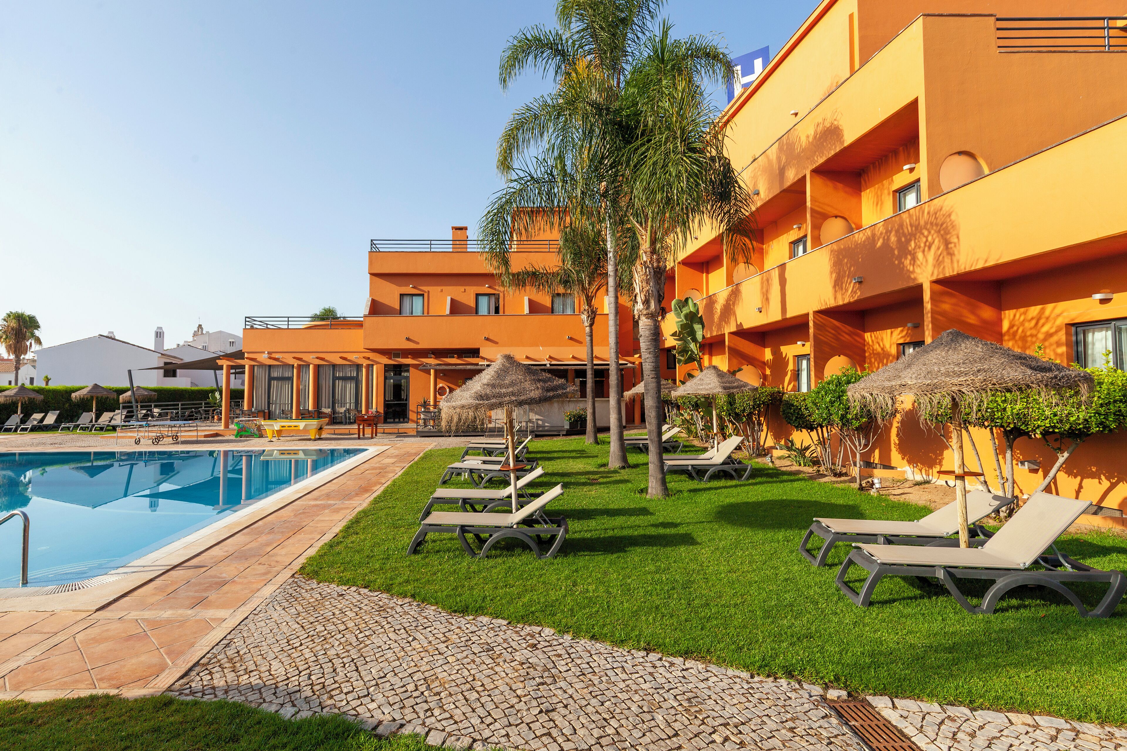 A hotel pool area with lounge chairs, palm trees, and a clear blue pool.