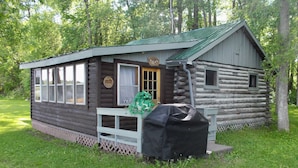 Une cabane en rondins avec un porche à l’avant, une porte et une fenêtre.