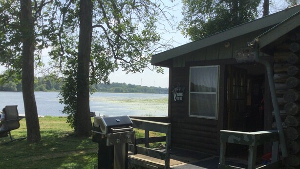 Une cabane avec un barbecue et un banc, située près d’un lac.