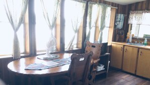 Une table à manger en bois, des chaises, un ventilateur et une fenêtre avec des rideaux.