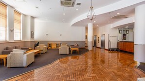 A spacious lobby with a herringbone wood floor, seating area with sofas and armchairs, a reception desk, and a modern chandelier. - Perth West End Apartment 406 (Perth)