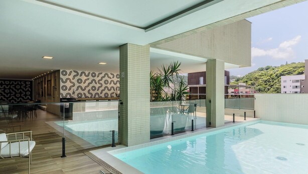 Una piscina interior moderna con una barrera de cristal, una zona de estar con sillones y una pared con diseño.
