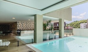 En modern inomhuspool med en glasvägg, ett område med sittplatser och stolar samt en vägg med ett mönster.