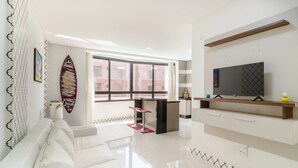 Una sala de estar moderna con un sofá, un televisor, una tabla de surf y un ventanal grande.