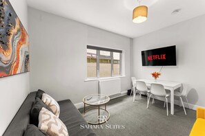 Un salon moderne comprenant un canapé, une table en verre, un coin repas avec des chaises, un téléviseur fixé au mur et une fenêtre donnant sur un beau paysage.