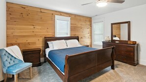 Quarto com cabeceira de madeira, cama com manta azul, mesa de cabeceira, cômoda e ventilador de teto.