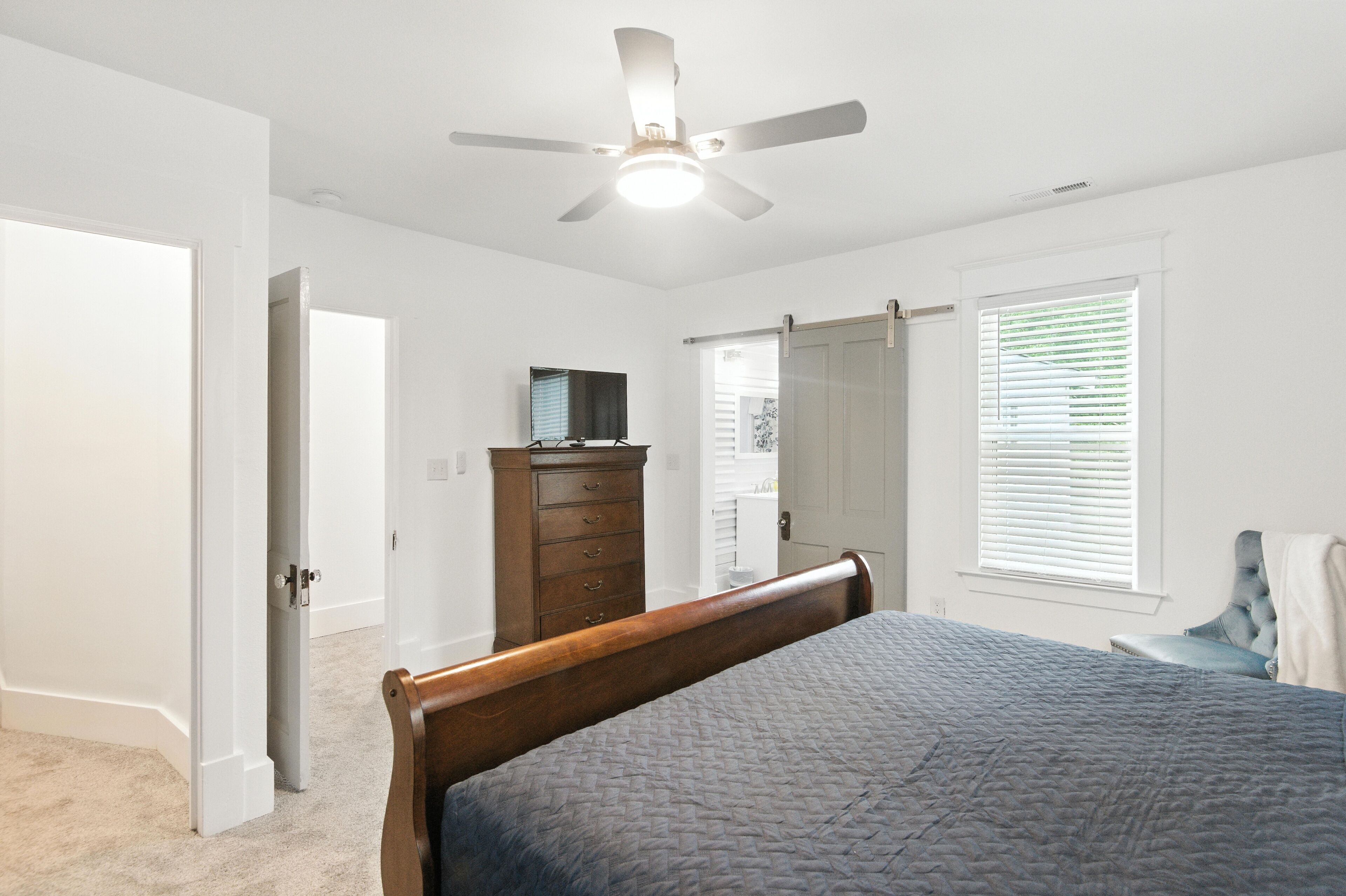 A bedroom with a bed, a dresser, a ceiling fan, and a window with blinds.