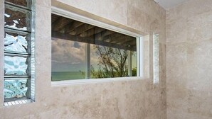 Una habitación con un amplio ventanal con vista a una playa, una pared de piedra y un techo de madera.