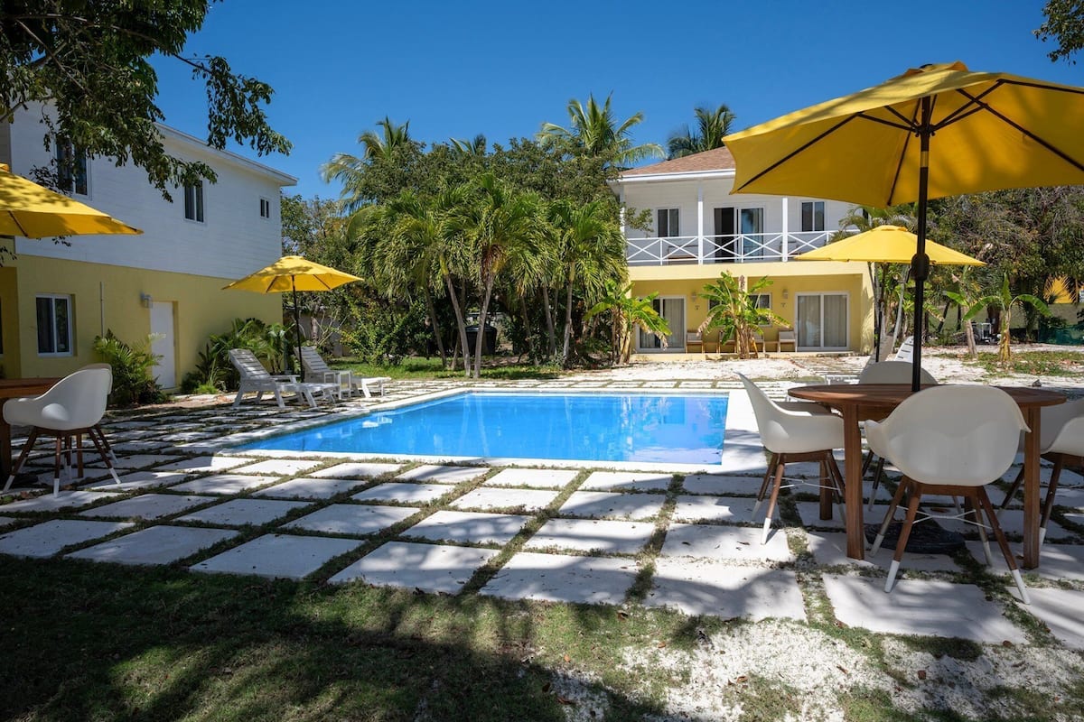 A pool area with a clear blue pool, surrounded by white lounge chairs and yellow umbrellas.