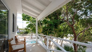 A covered outdoor area with a pool, wooden chairs, and a white railing. - Laughing Bird Studio #7 - Brand New Stylish Apartment, Pool, Bea 1 Bedroom Condo (Governor's Harbour)