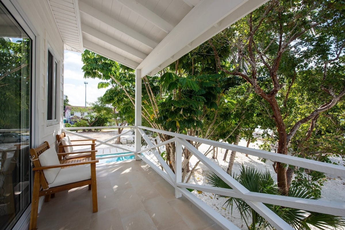 A covered outdoor area with a pool, wooden chairs, and a white railing.