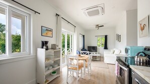 A modern kitchen with a dining area, a TV, and a large window overlooking greenery. - Laughing Bird Studio #7 - Brand New Stylish Apartment, Pool, Bea 1 Bedroom Condo (Governor's Harbour)