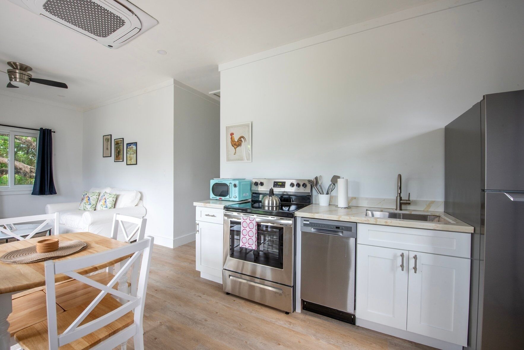 A modern kitchen with white cabinets, stainless steel appliances, a wooden dining table, and a window with curtains.