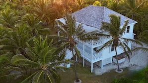 A white house with a tiled roof surrounded by palm trees, located near a body of water.