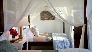 A bedroom with a canopy bed, a bedside table with a lamp, a vase of flowers, and a colorful artwork on the wall.