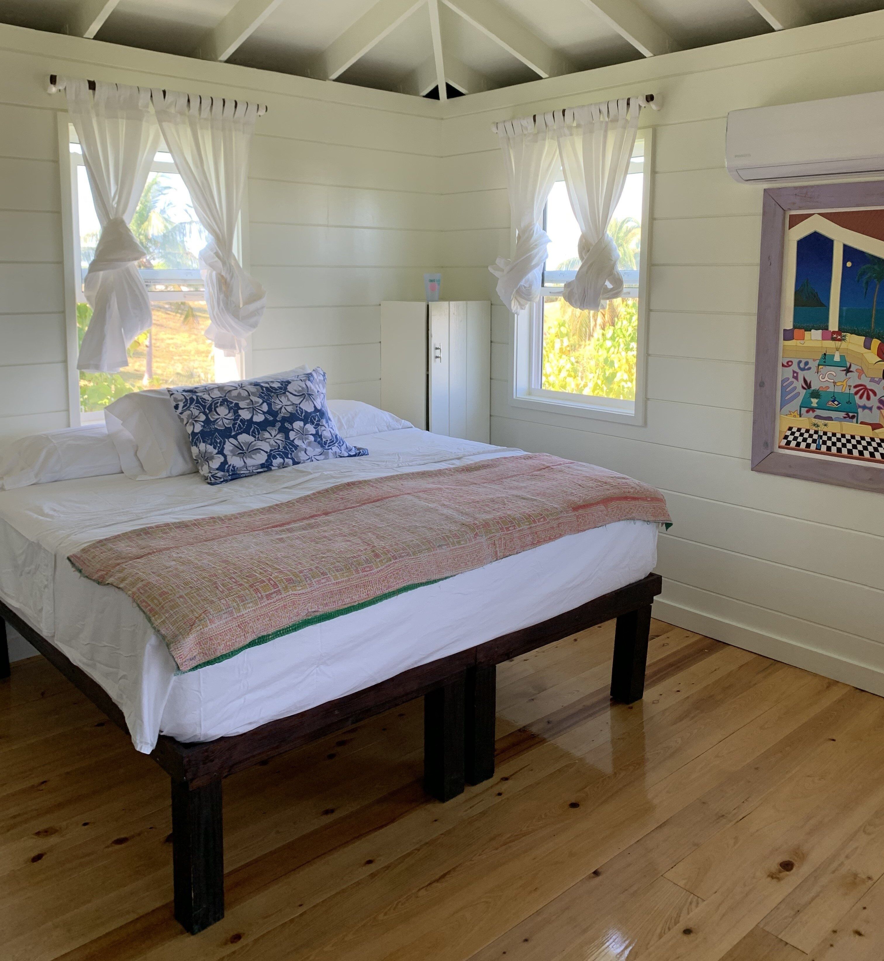 Une chambre à coucher avec un lit, des rideaux blancs, un plancher en bois et une fenêtre donnant sur un paysage verdoyant.