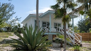 Ein Strandhaus mit weißer Fassade, einer Holzdielen-Terrasse und einer Treppe zu einer überdachten Veranda.