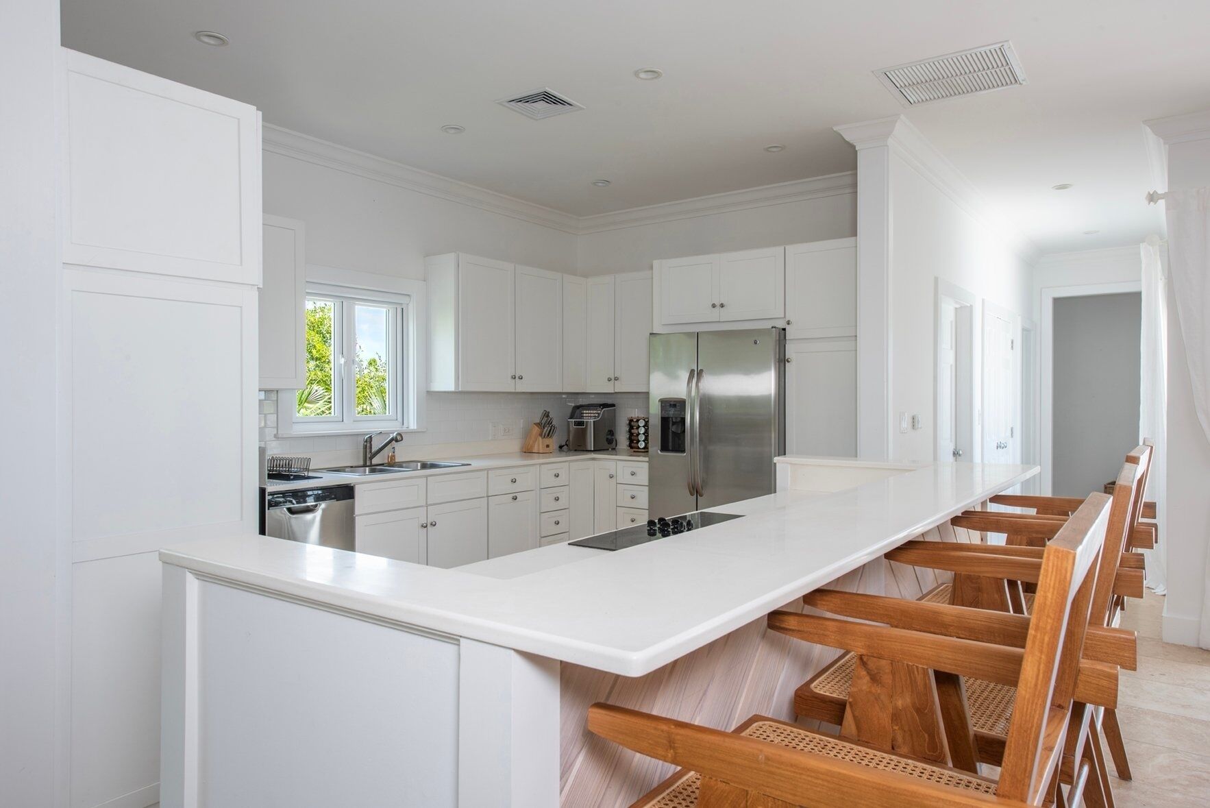 A modern kitchen with white cabinetry, a stainless steel refrigerator, and a wooden bar area.