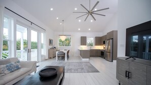 Un espacio de sala de estar moderno y diáfano, con una mesa de comedor, sofá y una cocina equipada con un refrigerador grande y un televisor de pantalla plana.