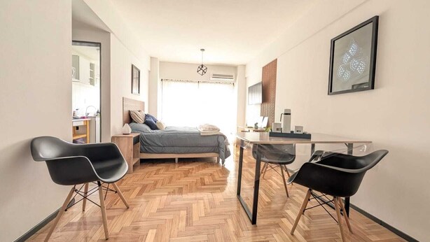 Ein modernes Schlafzimmer mit einem Bett, zwei schwarzen Stühlen, einem kleinen Tisch und einem Schreibtisch.