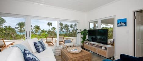 Amplia sala de estar con televisor grande, asientos cómodos y vista a palmeras.