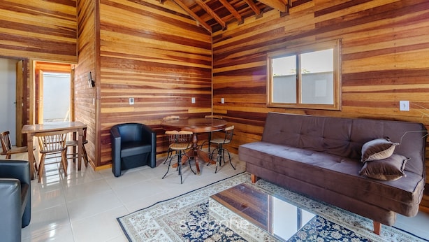 A wooden interior with a round dining table, a sofa, and a patterned rug.