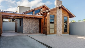 A modern house with a stone facade, wooden beams, and a covered patio area.