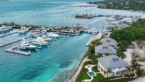 Un puerto deportivo con varios yates amarrados, un muelle y una zona residencial con casas y una piscina.