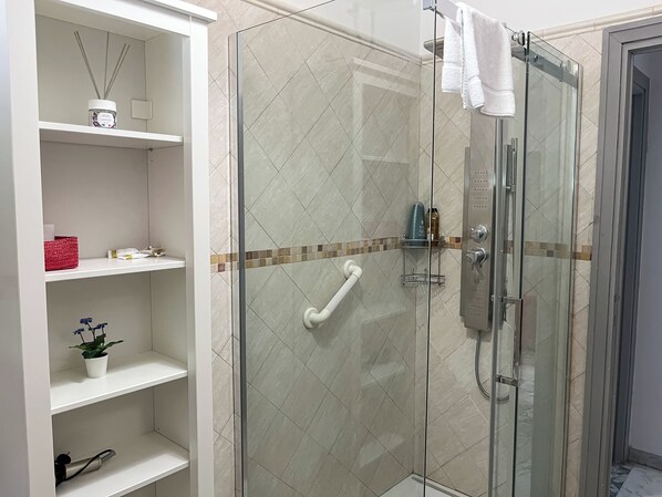 A modern bathroom with a glass-enclosed shower, white shelves, and a small potted plant.