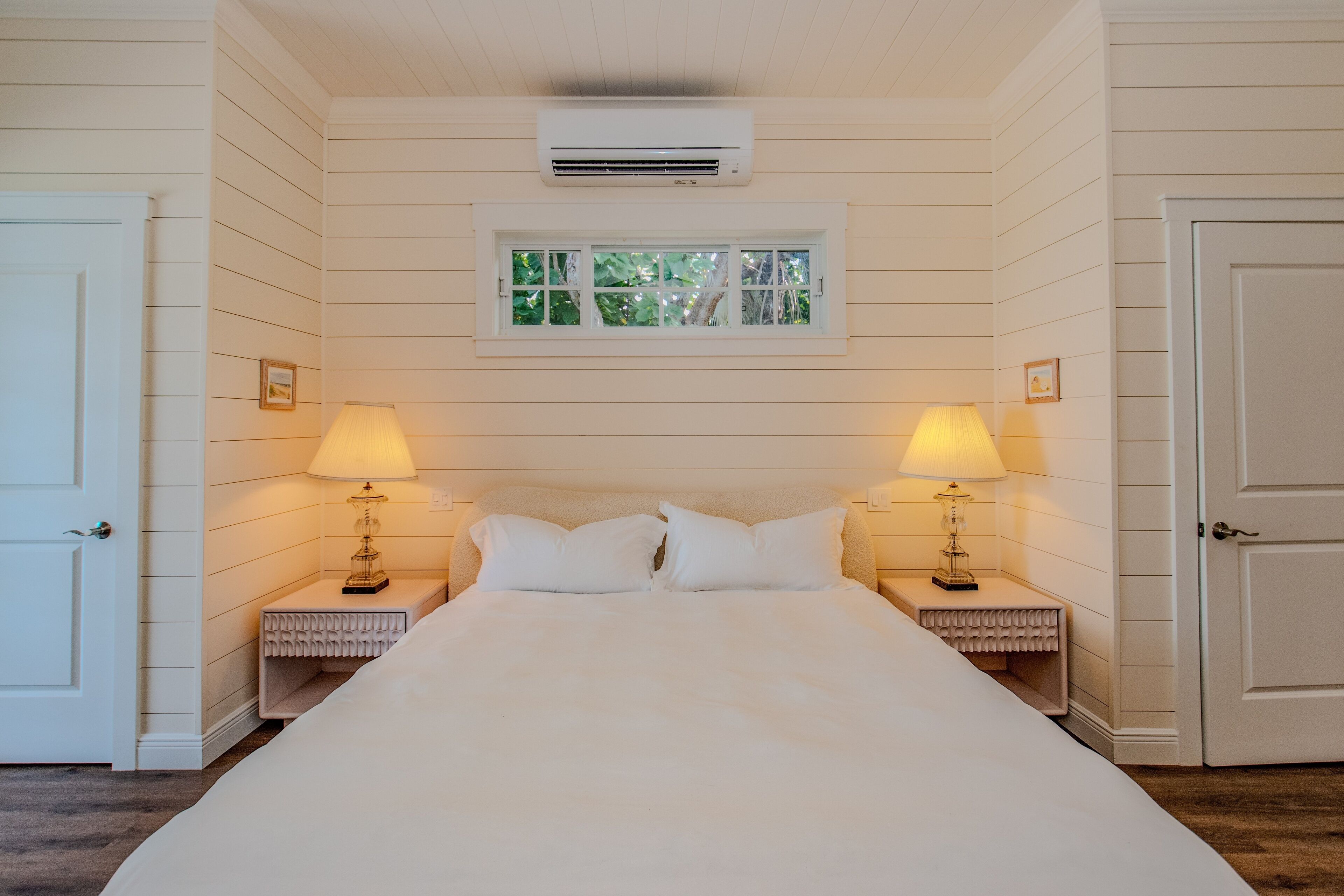 Une chambre dotée d’un grand lit, de deux tables de chevet avec des lampes, d’une fenêtre offrant une belle vue et d’un appareil de climatisation.