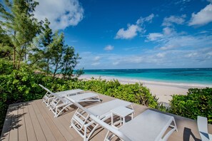 Eine Terrasse mit weißen Liegestühlen und Tischen mit Blick auf einen Strand, der klares türkisblaues Wasser und einen Sandstrand bietet.