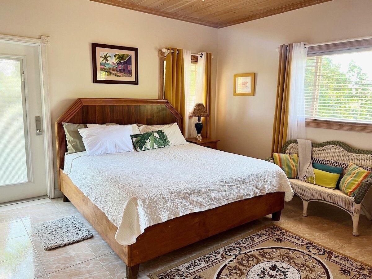 Un dormitorio con una cama de madera, una silla de mimbre, un tapiz estampado y una ventana con cortinas.
