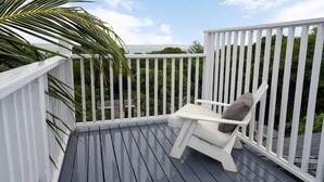 Een terras met een witte reling, een witte stoel met kussen en een palmboom.