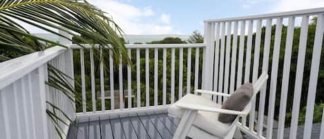 A deck with a white railing, a single white chair with a cushion, and a palm tree.