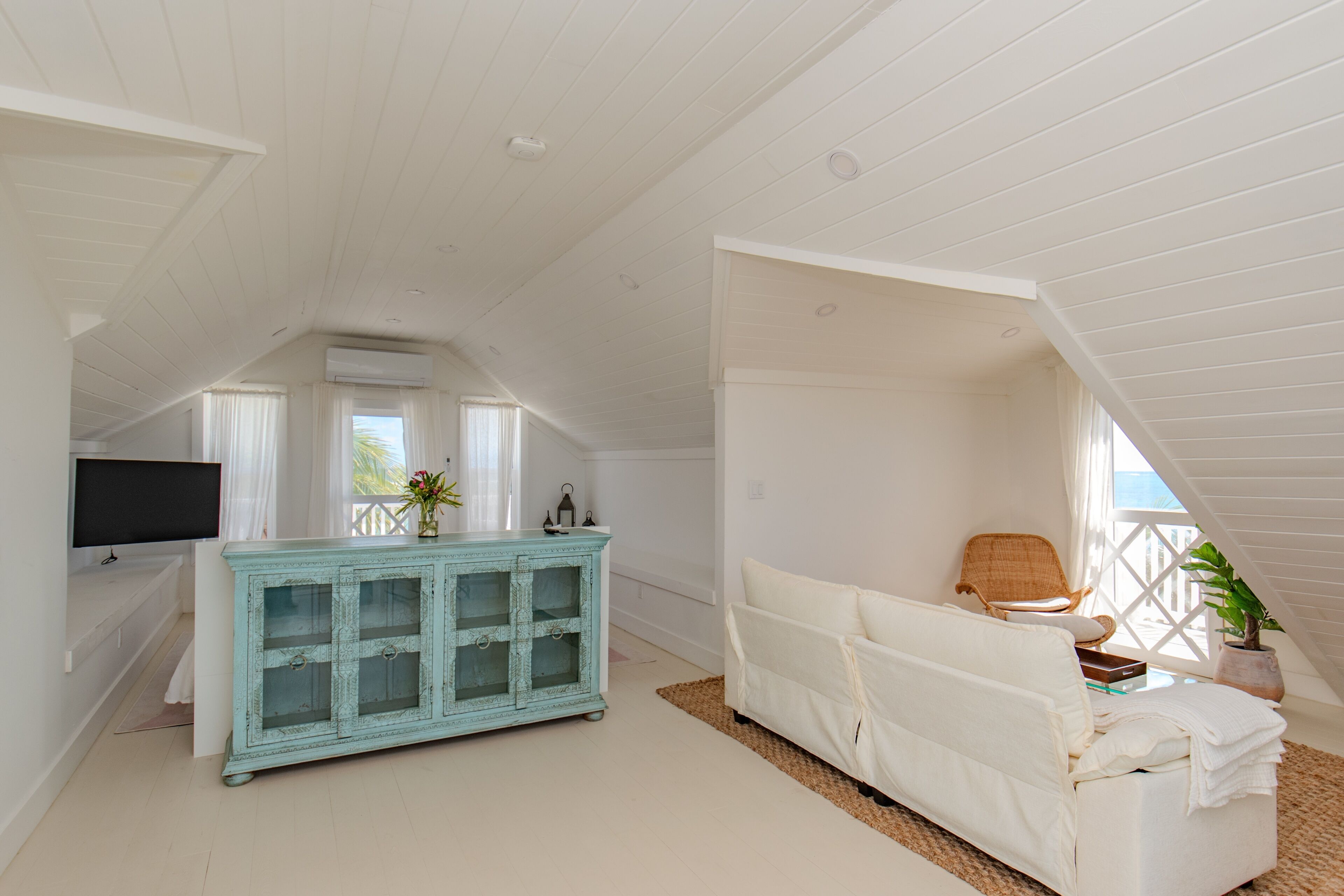 A spacious room with a high ceiling, a white sofa, a turquoise cabinet, and a television on the left wall.