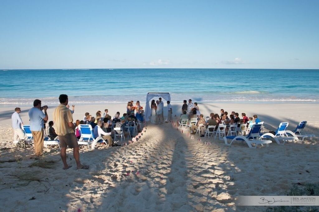 Eine Strandhochzeitszeremonie, bei der Gäste Stühle sitzend dem Altar zugewandt haben.