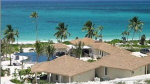 A beachfront property with thatched-roof buildings, a pool, and palm trees. - Sky Beach Club Bungalow 3 Steps From Beach W/ Club, Pool 1 Bedroom Bungalow (Governor's Harbour)