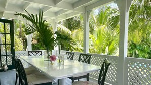 A covered outdoor patio with a white table and chairs, surrounded by lush tropical plants. - Hibiscus Hill Kings Treat - Ultimate Island Style House W/pool 3 Bedroom Home (Dunmore Town)