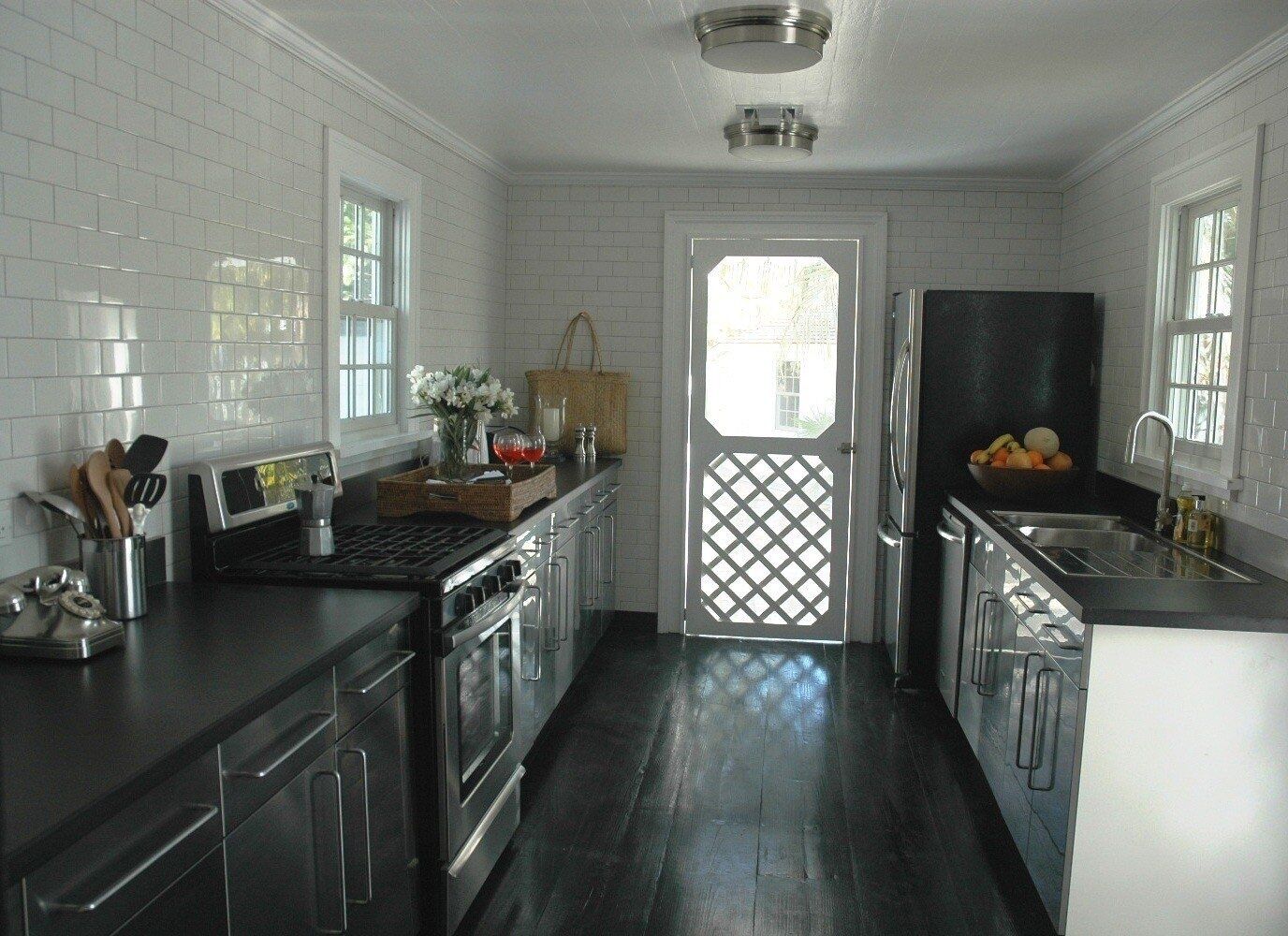 A modern kitchen with white subway tiles, stainless steel appliances, and a dark wooden floor.