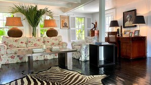 A living room with a sofa, coffee table, and a zebra rug. There are lamps, a plant, and a framed picture on the wall. - Hibiscus Hill Kings Treat - Ultimate Island Style House W/pool 3 Bedroom Home (Dunmore Town)