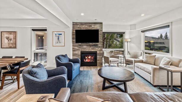 A modern living room with a fireplace, comfortable seating, and large windows offering a view of the outdoors. - Dulany Style+Comfort~Base Area Condo~Best Location (Steamboat Springs)
