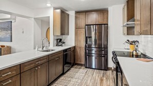 A modern kitchen with wooden cabinets, stainless steel appliances, and a white countertop. - Dulany Style+Comfort~Base Area Condo~Best Location (Steamboat Springs)