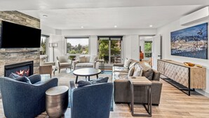 A modern living room with a fireplace, comfortable seating, a dining area, and a large window offering a view of the outdoors. - Dulany Style+Comfort~Base Area Condo~Best Location (Steamboat Springs)