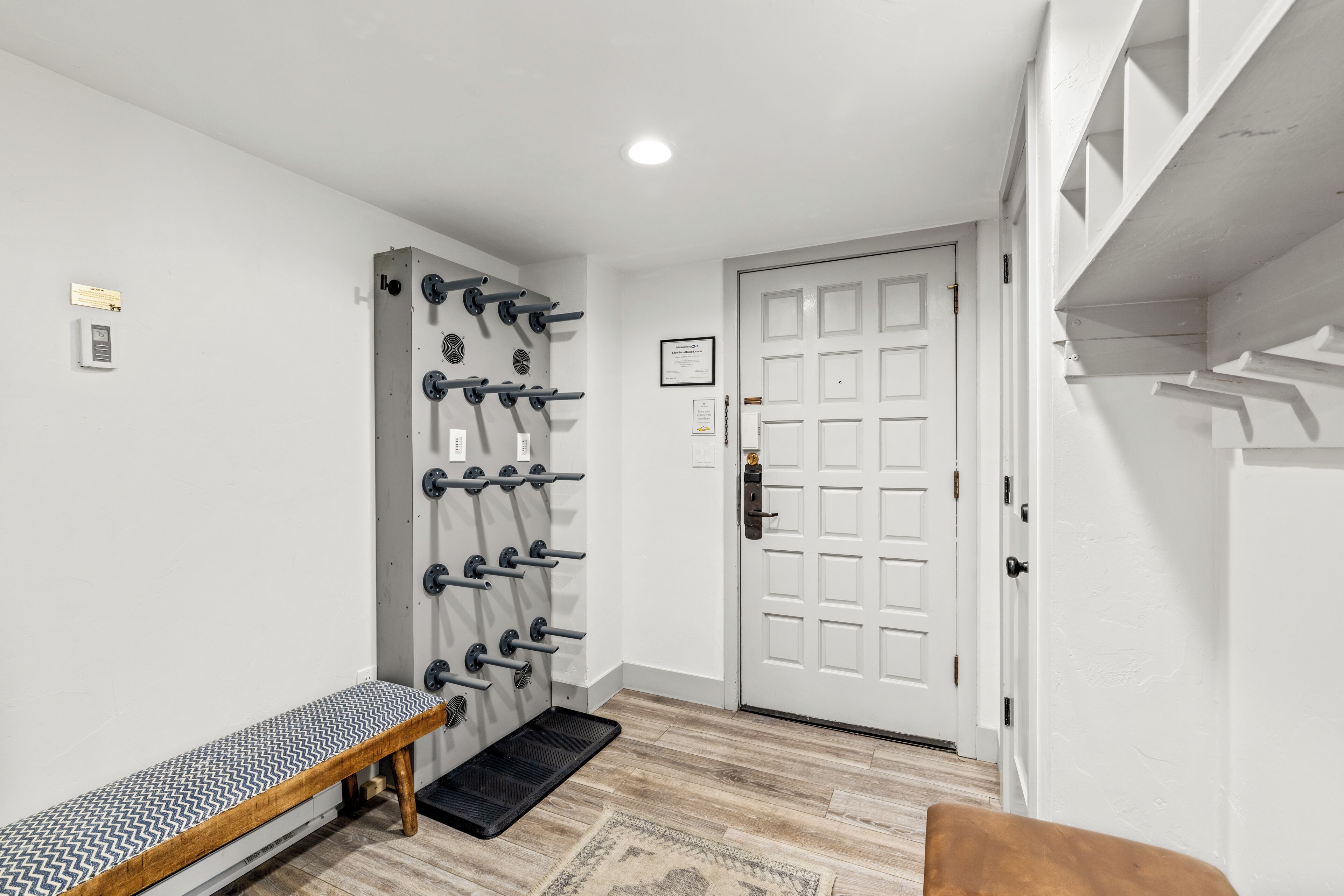 A room with a bench, a wall-mounted rack, a door, and a shelf.