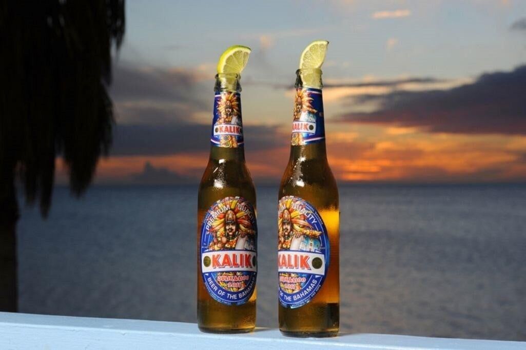 Two bottles of Kalik beer with a sunset view in the background.