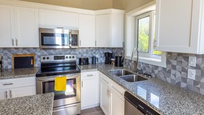 A modern kitchen with white cabinets, stainless steel appliances, granite countertops, and a window providing natural light. - Seas The Day - Brand New Villa W/ocean View, Walk To Rainbow Bea 3 Bedroom Home (Rainbow Bay)